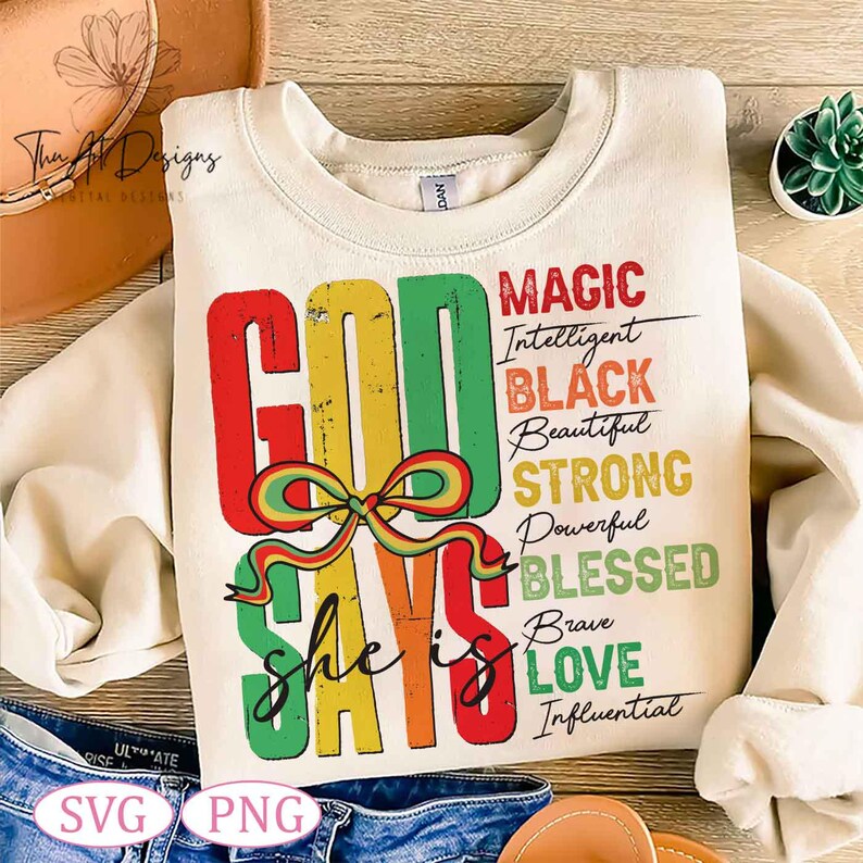 Op de afbeelding: Een cr&egrave;mekleurig sweatshirt met een kleurrijk grafisch ontwerp dat "God Says She Is" zegt met de woorden "Magic, Intelligent, Black, Beautiful, Strong, Powerful, Blessed, Brave, Love, Influential" in zwarte tekst.