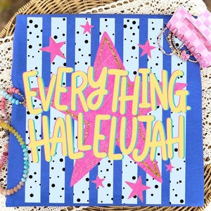 以下が含まれることがあります： 青い背景に、垂直の青いストライプと黒い水玉模様。 「EVERYTHING. HALLELUJAH」の文字は黄色で、黒い縁取りがあり、金色のグリッターアクセントが付いたピンクの星の上に配置されています。 ピンクの星のアクセントがテキストの周りに散らばっています。