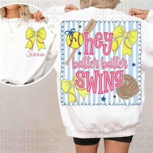 May include: White sweatshirt with a softball theme. The front features a yellow bow and softball graphic with the name "Jessie" in pink. The back has a blue and white striped design with the words "hey batter batter SWING".