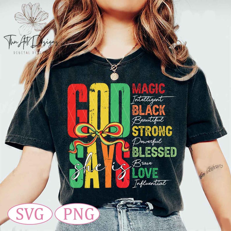 Op de afbeelding: Een zwart T-shirt met een kleurrijk grafisch ontwerp dat "God zegt dat ze is" zegt met een lijst van positieve eigenschappen, waaronder "Magie, Intelligent, Zwart, Mooi, Sterk, Krachtig, Gezegend, Dapper, Liefde, Invloedrijk".