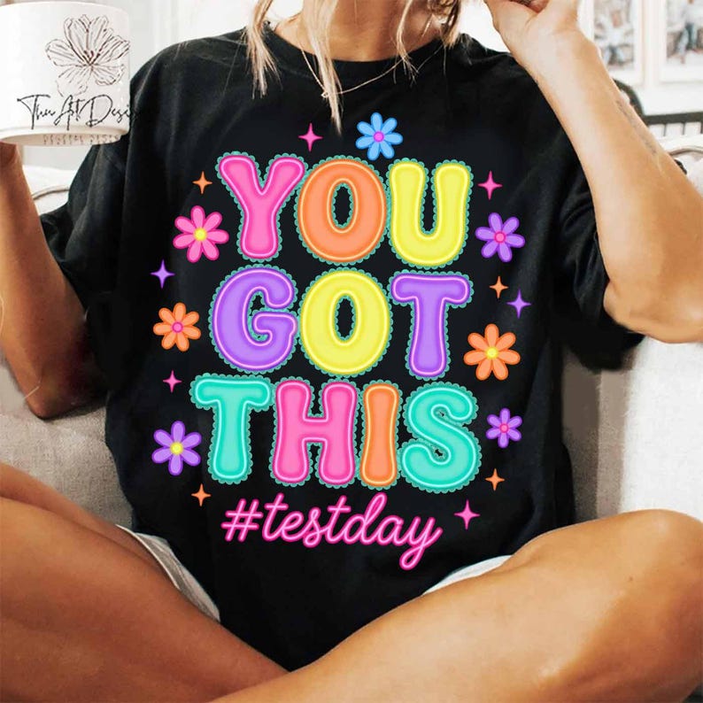 Pode incluir: T-shirt preto com a frase "YOU GOT THIS" em letras coloridas, decorado com flores e estrelas. A hashtag "#testday" est&aacute; escrita abaixo em rosa.