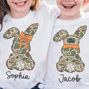 May include: Two white t-shirts with a camouflage bunny rabbit design. One shirt says "Sophia" and the other says "Jacob". The bunny on the "Jacob" shirt is wearing a hat that says "Egg Hunter".