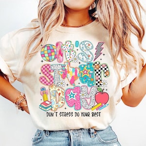May include: A white t-shirt with a colourful graphic that says "It's School Day" with a variety of colourful patterns and designs. The text "Don't Stress Do Your Best" is printed below the graphic.