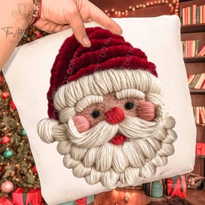 May include: A white square pillow featuring a detailed Santa Claus face. The Santa face is made of textured yarn in red, white, pink, and black. The Santa hat is a deep red, and the beard is a fluffy white. The pillow is a festive Christmas decoration.