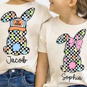 May include: Two white t-shirts with a checkered Easter bunny design. One shirt has a blue and orange hat with the text "egg hunter" and the name "Jacob". The other shirt has a pink bow and the name "Sophia".