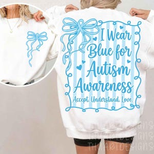 May include: White sweatshirt with a light blue bow graphic on the front and back. The back features the text "I Wear Blue for Autism Awareness. Accept. Understand. Love." in light blue. The design includes blue stripes and hearts.
