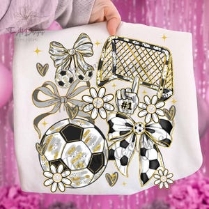 May include: A white graphic design featuring soccer-themed elements. Includes soccer balls, a goal, bows, daisies, hearts, and a #1 foam finger. Accents are gold and gray.