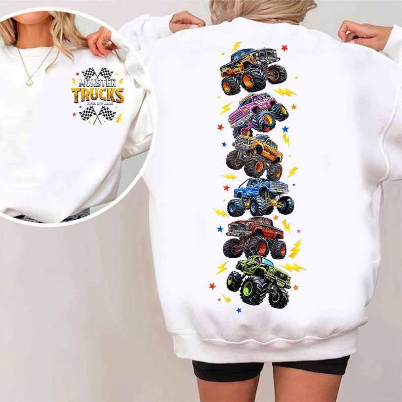 Puede incluir: Sudadera blanca con un gr&aacute;fico colorido de monster trucks. La parte delantera presenta el texto "Monster Trucks Are My Jam" con banderas a cuadros y rayos. La parte trasera muestra una fila vertical de ilustraciones de monster trucks.