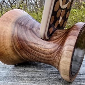 Op de afbeelding: Een houten telefoonstandaard met een uniek, swirlend houtnerfpatroon. De standaard is gemaakt van donkerbruin hout en heeft een gladde, gepolijste afwerking.