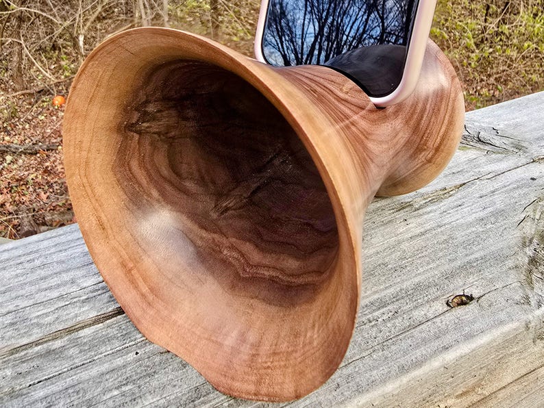 Op de afbeelding: Een houten versterker gemaakt van &eacute;&eacute;n stuk hout, ontworpen om geluid van een smartphone te versterken. De versterker is hoornvormig en heeft een natuurlijke houten afwerking.