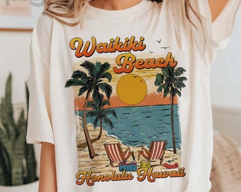 Puede incluir: Camiseta color crema con un gráfico retro de Waikiki Beach en Honolulu, Hawái. El diseño incluye palmeras, una puesta de sol, sillas de playa y el texto "Waikiki Beach Honolulu Hawaii" en una fuente vintage.
