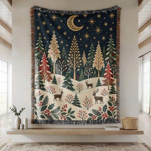 May include: A woven throw blanket featuring a dark blue night sky with a crescent moon and stars above a snowy forest landscape. The scene includes stylized evergreen trees, red berry bushes, and two deer standing on white hills with fringe edges.