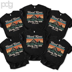 May include: Black t-shirts with a retro design featuring the text "Hood River" above a mountain scene with the words "Family Trip 2026" and "Custom Name". The design includes orange, teal, and green colors.
