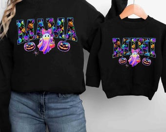 May include: Black sweatshirts with Halloween designs. One says "MAMA" and the other "MINI" in a colourful, patterned font. Both feature ghost, pumpkin, and spider graphics, perfect for matching outfits.