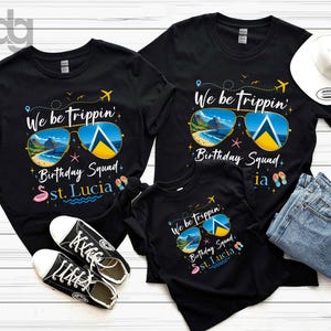 May include: Black t-shirts with the text "We be trippin' Birthday Squad St. Lucia" and sunglasses graphic. The image includes a white hat, blue jeans, and black sneakers. The sunglasses graphic features a beach scene and the St. Lucia flag.