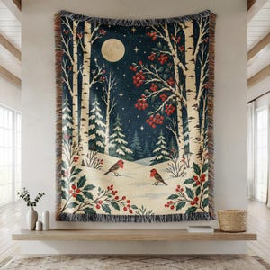 Könnte beinhalten: Eine gewebte Wohndecke mit einer winterlichen Nachtszene, Vollmond, Sternenhimmel, verschneitem Boden, Birken und roten Beeren. Zwei kleine Vögel mit roter Brust stehen im Schnee. Die Decke ist an allen Seiten mit Fransen versehen.