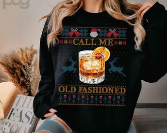 Op de afbeelding: Zwart sweatshirt met een feestelijk ontwerp met een cocktailglas, rendieren en de tekst "CALL ME OLD FASHIONED". Het ontwerp bevat een kers en een sinaasappelschijfje als garnering.