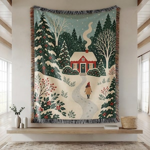 May include: A woven throw blanket featuring a winter scene with a red cottage, snow-covered pine trees, and a person walking along a path. The design includes holly bushes with red berries, a light blue sky, and a fringed edge on all four sides.