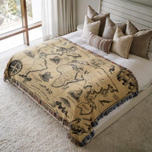 May include: A tan throw blanket with a vintage world map design. The map features detailed illustrations of continents, oceans, and nautical elements. The blanket has a fringed edge and the text "VINTAGE WORLD MAP".