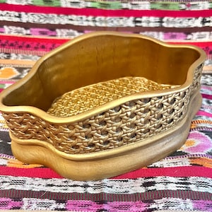 May include: A gold-colored decorative bowl with a woven pattern. The bowl has a wavy, organic shape and a smooth, glossy finish.