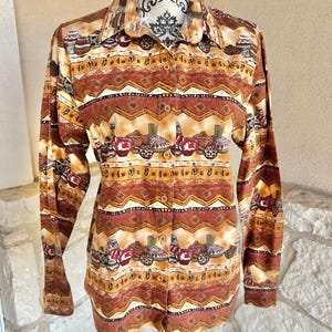 May include: A button-down shirt with a Southwestern-inspired pattern. The long-sleeved shirt features a repeating design of pottery and geometric shapes in shades of brown, tan, and red. The shirt is displayed on a mannequin.