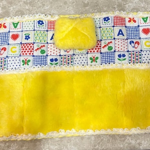 May include: A yellow plush baby blanket with a patchwork fabric panel featuring letters, hearts, and butterflies. The panel has a white lace trim.
