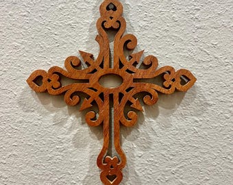 May include: A wooden cross with an ornate, openwork design. The cross is a warm brown color and features intricate scrollwork and a central oval. The cross is likely intended for wall decor.