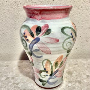 May include: A white ceramic vase with a pink rim and hand-painted floral designs in shades of pink, orange, blue, and green.
