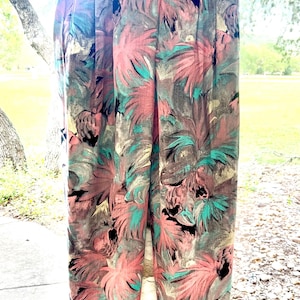 May include: High-waisted pants with a colorful floral pattern. The pants feature a mix of pink, teal, and black against a muted background. The pants are hanging on a wooden hanger.