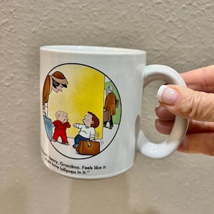 May include: A set of three ceramic mugs with a speckled, cream-colored glaze. Each mug features a different hand-painted design: a blue and green leaf, a yellow flower, and a red berry. The mugs have a simple, modern design.