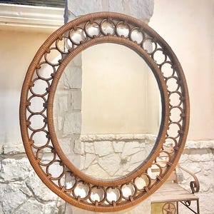 May include: A large circular wall mirror featuring a brown rattan frame. The frame is constructed with a thick outer ring and an inner ring, connected by a series of smaller, evenly spaced circular rattan loops that create an openwork design.