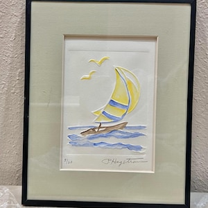May include: Framed artwork featuring a sailboat with a yellow sail and blue stripes, sailing on blue waves. Two yellow birds fly above. The artwork is signed "P. Hagstrom" and numbered 3/20. The frame is black with a light green mat.