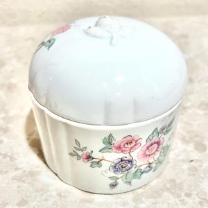 May include: White ceramic jar with a floral design. The lid has a raised floral knob. The jar has a fluted design on the bottom half.