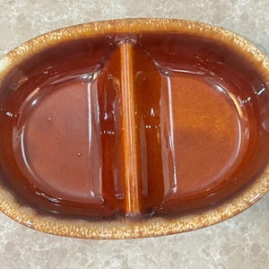 May include: An oval-shaped, divided serving dish with a glossy, brown interior and a lighter, speckled rim. The dish is divided into two sections by a central divider, perfect for serving snacks or appetizers.