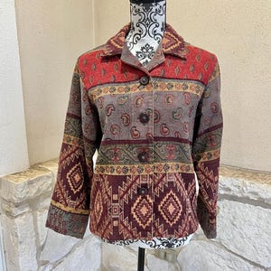 Puede incluir: Una chaqueta tejida multicolor con un patrón de paisley y geométrico. La chaqueta tiene un frente abotonado y mangas largas.