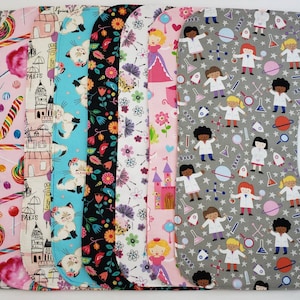 May include: A set of ten fabric bibs with different patterns. The bibs are all in a similar shape, with a rounded neck and a pointed bottom. The patterns include candy, a castle, cats, flowers, a princess, and scientists.