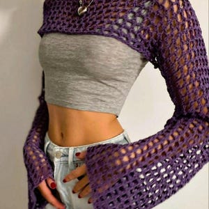 May include: A purple crochet top with long sleeves and a cropped design. The top is made of a lightweight, open-weave fabric.