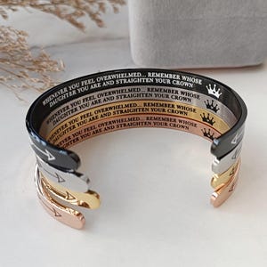 May include: Four stacked bracelets with a silver, gold, rose gold, and black finish. Each bracelet has the inscription "Whenever you feel overwhelmed... Remember whose daughter you are and straighten your crown."  The inscription is in black lettering on each bracelet.
