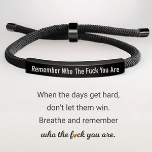 May include: Black adjustable bracelet with the text "Remember Who The Fuck You Are". The bracelet is made of a black rope-like material and features a black metal bar with the inscription. The image also includes inspirational text.