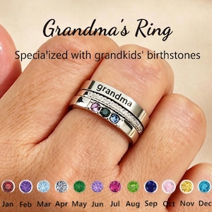 Pode incluir: Um conjunto de anéis prateados com o texto Grandma, uma banda com pedras claras incrustadas e uma banda com três pedras de nascimento redondas em roxo, verde escuro e azul. Abaixo, uma tabela mostra doze pedras de Jan a Dez.