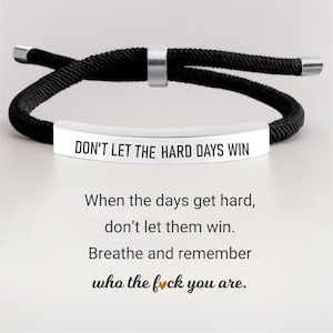 May include: A black rope bracelet with a silver metal bar inscribed with "DON'T LET THE HARD DAYS WIN". A motivational bracelet with a black rope design and a silver clasp.