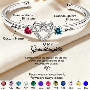 May include: A silver-toned cuff bracelet featuring a central heart motif encrusted with small clear stones, flanked by a red and a blue circular gemstone. The band is engraved with the names Jessica and Grace. Text includes TO MY Granddaughter.