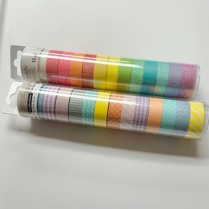 May include: Two clear plastic tubes of decorative crafting tape. One tube contains rainbow-colored tapes, including glitter and solid colors. The other tube has patterned tapes in pastel colors. The tubes are labeled with the brand name and the number of pieces.