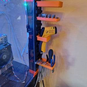 May include: Orange wall-mounted organizer with shelves for tools. A yellow laser thermometer is hanging on the left side. The right side has a rack for holding screwdrivers and pliers.