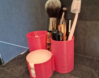 Può includere: Organizzatore per trucco in plastica rosa con quattro scomparti. L'organizzatore contiene una varietà di pennelli per il trucco, tra cui un pennello grande e soffice, un pennello più piccolo e un pennello eyeliner nero. L'organizzatore contiene anche uno spazzolino da denti rosa e una piccola bottiglia di liquido.