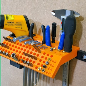 Puede incluir: Organizador de herramientas naranja con una variedad de herramientas, incluyendo destornilladores, llaves Allen y un calibre digital. El organizador tiene una etiqueta que dice "PEREL EEM100 Termómetro infrarrojo".