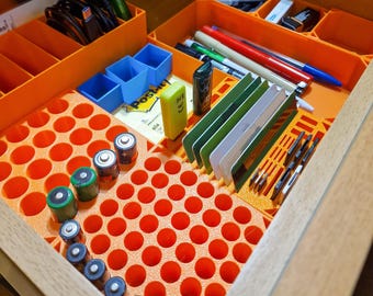 May include: An orange drawer organizer with compartments for batteries, SD cards, and other small items. The organizer also includes a sticky note with the word "Post-it" on it.