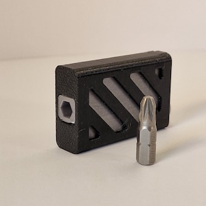 May include: A black plastic case with a grey patterned insert holds a silver screwdriver bit with the text "ECR - VPZ3" on the side.