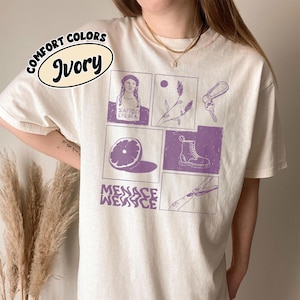 Könnte beinhalten: Elfenbeinfarbenes T-Shirt mit einem lila Grafikdesign. Das Design umfasst eine Büste, einen Zweig, Schlüssel, eine halbe Orange, einen Stiefel und den Text "MENACE WEAVCE". Das Shirt ist mit "COMFORT COLORS" und "Ivory" gekennzeichnet.