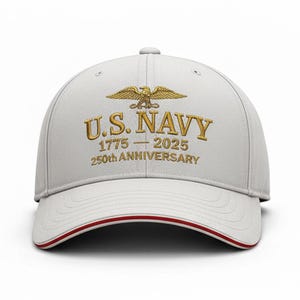 May include: A white baseball cap with a curved brim and a red trim. The cap features gold embroidered text and an eagle design, reading "U.S. NAVY 1775-2025 250th ANNIVERSARY".